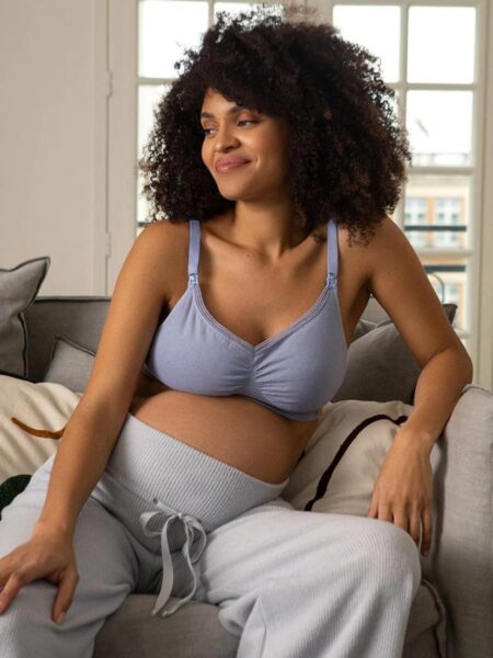 Mother wearing a non-toxic organic cotton nursing bra during postpartum recovery in a bright natural bedroom.