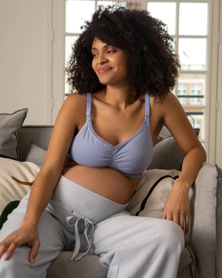 Mother wearing a non-toxic organic cotton nursing bra during postpartum recovery in a bright natural bedroom.